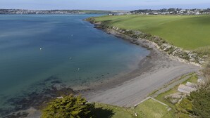 A coastal landscape with a clear view of the sea, a sandy beach, and a grassy area with a few buildings in the distance. - Schoopers is set amongst rolling green fields on the edge of the Camel Estuary. (Wadebridge)