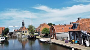 A canal-side building with a traditional brick facade, a visible entrance, and a small outdoor seating area with tables and chairs.