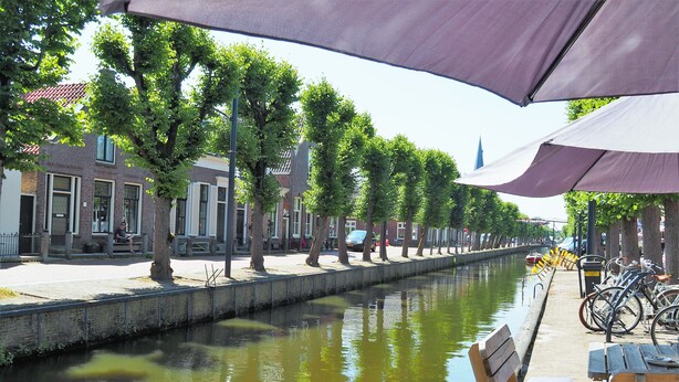 A canal-side walkway with benches and umbrellas, lined with trees and buildings.