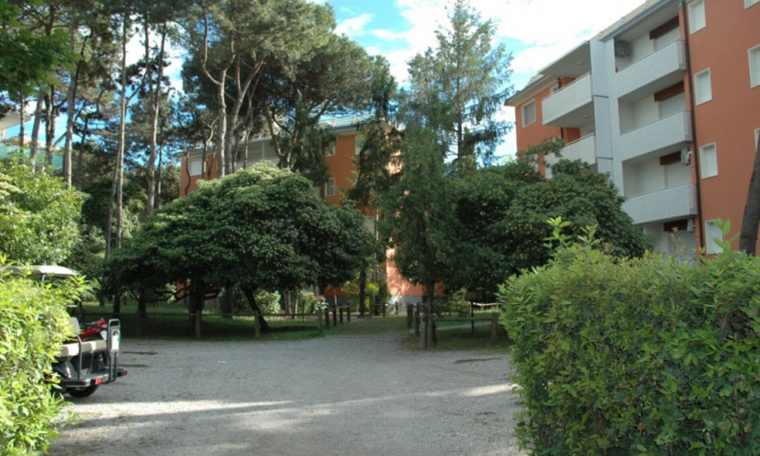 Un cortile con un vialetto sterrato, circondato da alberi e un edificio a più piani con balconi.