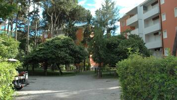 Un cortile con un vialetto sterrato, circondato da alberi e un edificio a più piani con balconi.