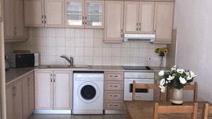 Une cuisine moderne avec des meubles en bois clair, un lave-linge encastré et un coin repas comprenant des chaises et une table en bois.