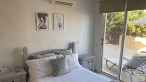 Une chambre à coucher avec un lit, des tables de chevet et une vue sur un espace extérieur comprenant une chaise et un parasol.