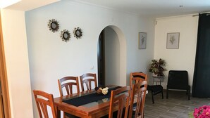 Zona de dinar amb taula i cadires de fusta, un cal·lís negre i tres objectes decoratius penjats a la paret.