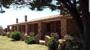 A stone building with a tiled roof, surrounded by greenery and a large tree. - Gallura House Sardinia (trinita d agultu e vignola)