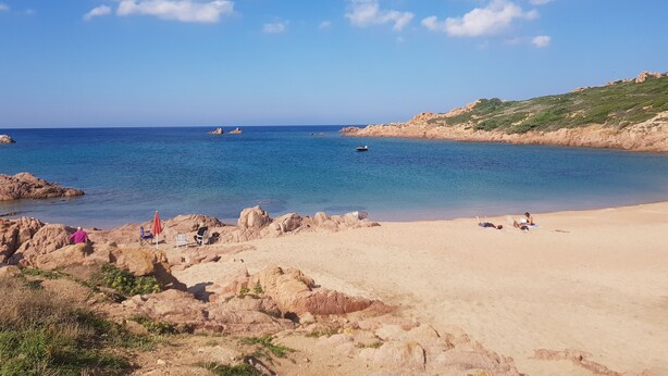 A beach with clear blue water, rocky formations, and a few people relaxing. - Gallura House Sardinia (trinita d agultu e vignola)