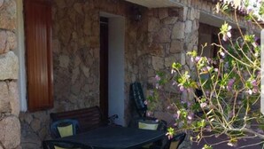An outdoor dining area with a stone wall, a table with chairs, and a small tree with pink flowers. - Gallura House Sardinia (trinita d agultu e vignola)