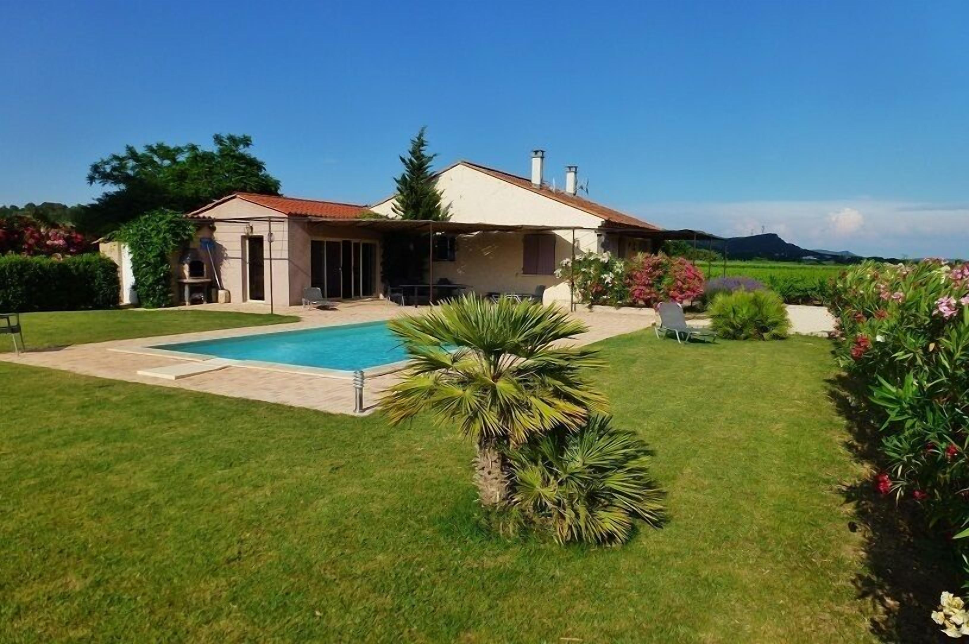 Une maison avec une piscine, une terrasse et un jardin agrémenté de diverses plantes et fleurs.