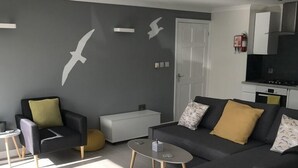 A modern living room with a grey sofa, a glass coffee table, and a white armchair. - Beautiful Modern SeaView Apartment in WatergateBay (Newquay)
