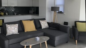 A modern living room with a grey sectional sofa, a small round coffee table, and a black floor lamp. - Beautiful Modern SeaView Apartment in WatergateBay (Newquay)