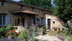 A rustic house with a stone extension, a gravel driveway, and a variety of flowering plants. - Petit Vue Vert - One  Bedroom Gite with heated pool on edge of medieval village (Puy-l'Évêque)