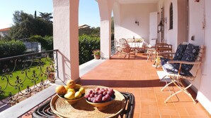 Eine Terrasse mit Korbmöbeln, einem Tisch mit Früchten und Blick auf Grünflächen und Gebäude.