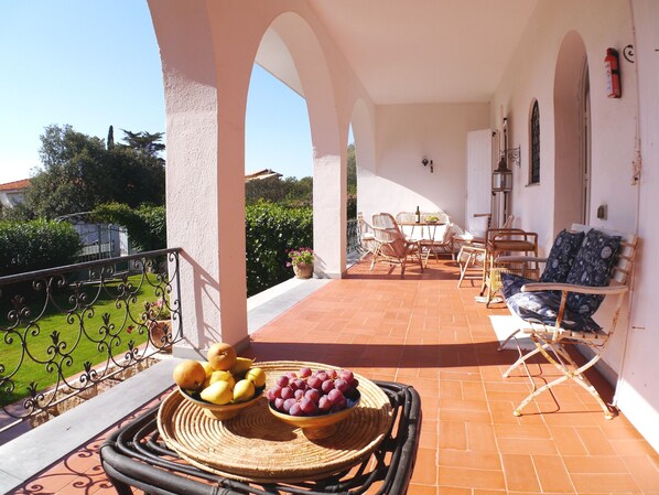 A terrace with wicker furniture, a table with fruit, and a view of greenery and buildings.