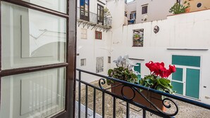 A balcony with a metal railing, a white building with a green door, and red flowers in a pot. - Torremuzza Home by Wonderful Italy (Palermo)