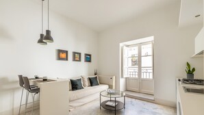 A modern living room with a sofa, a coffee table, and a dining area with chairs. There are framed pictures on the wall and a large window providing natural light. - Torremuzza Home by Wonderful Italy (Palermo)