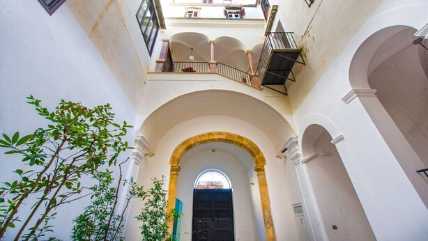A courtyard with a central archway, a black door, and a view of the sky through the arch. - Torremuzza Home by Wonderful Italy (Palermo)