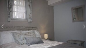 Un dormitorio con cama, mesita de noche, lámpara y ventana con cortinas.