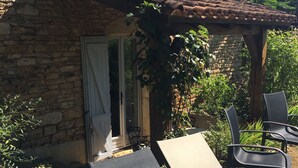 Un edificio de piedra con tejado de tejas, un porche cubierto y zona de estar al aire libre con sillas y una mesa.