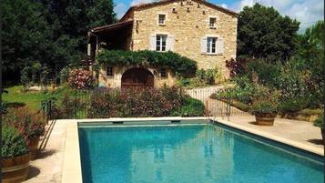 A stone building with a pool, surrounded by lush greenery and flowering plants.