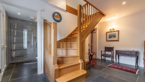 Eine Treppe führt zu einer zweiten Etage, ein Holztisch, ein Stuhl, ein gerahmtes Bild an der Wand und ein Duschbereich.
