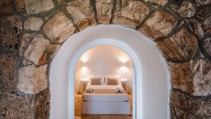 Una habitación con paredes de piedra, una cama, una mesita de noche y una lámpara.