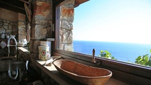 Cocina rústica con pared de piedra, encimera de madera, cesta tejida y vista al mar.