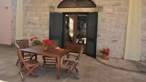 An outdoor wooden table with chairs, potted plants, and a door with shutters. - Typical Salento residence (Alessano)