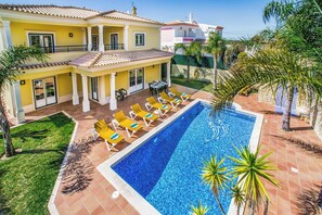 Un edificio amarillo de dos pisos con piscina, tumbonas y palmeras.