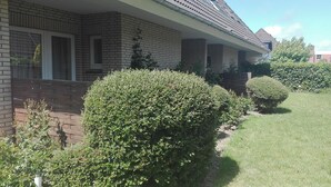 Une maison d’habitation avec une façade en briques, un porche à l’avant et des haies bien entretenues.
