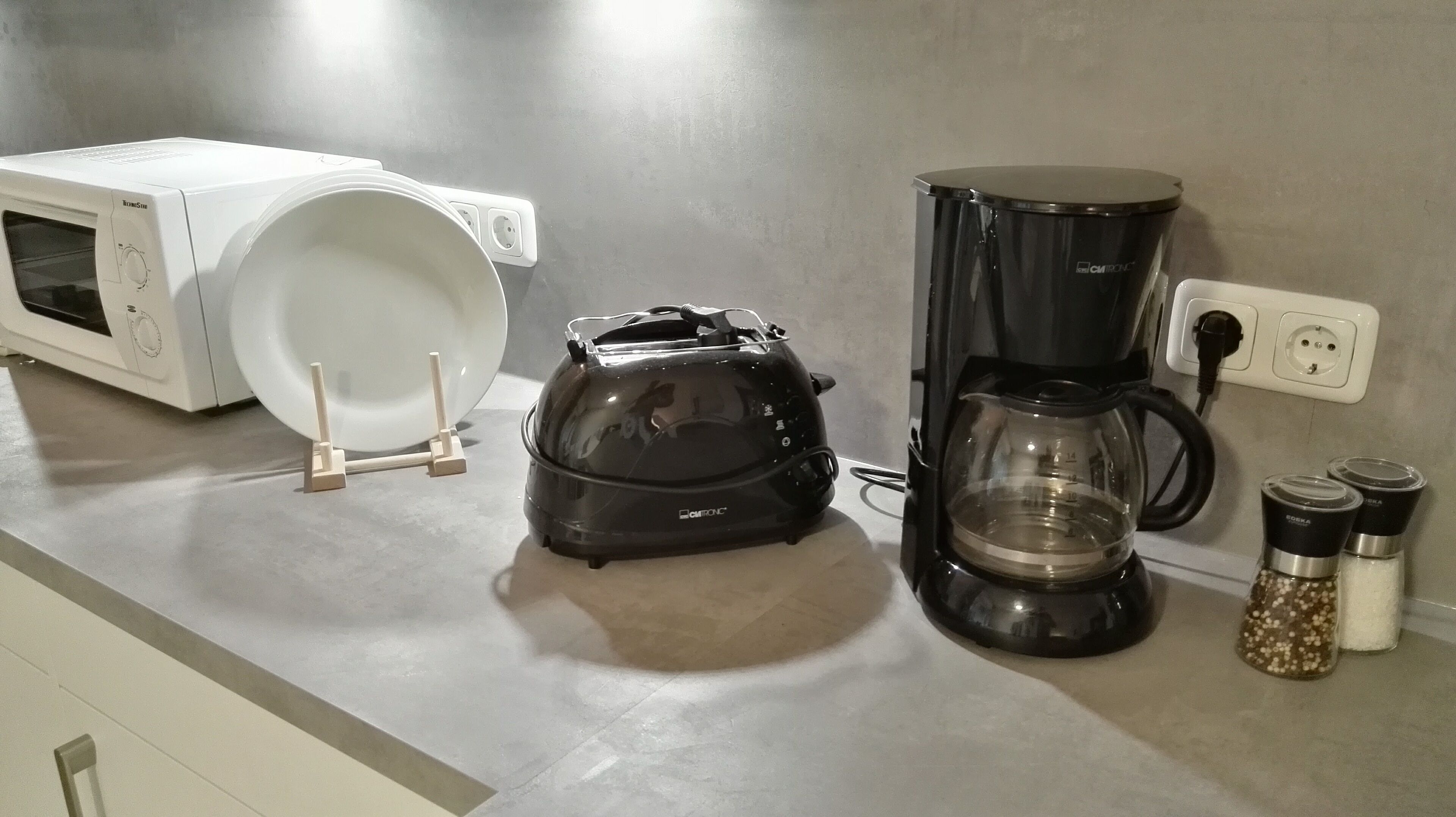 Una cocina con microondas, tostadora, cafetera y saleros y pimenteros en la encimera.