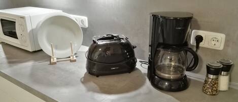 Una cocina con microondas, tostadora, cafetera y saleros y pimenteros en la encimera.