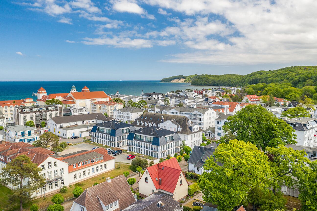 Une ville côtière où se côtoient des bâtiments résidentiels et commerciaux, dont un imposant bâtiment blanc surmonté d’un toit rouge et devant lequel se dresse un grand arbre.
