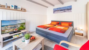 Un dormitorio moderno con una cama, un televisor, una mesita con una planta y una silla roja.