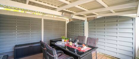 A covered patio area with a table set for dining, surrounded by wicker chairs.