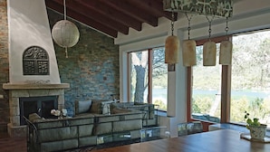 A cozy living room with a stone fireplace, a wooden dining table, and a large window overlooking a lake.