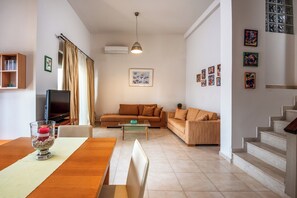 A living room with a sofa, a coffee table, a TV, and a staircase. - Blue Wave Villa up to 10 (RHODES)