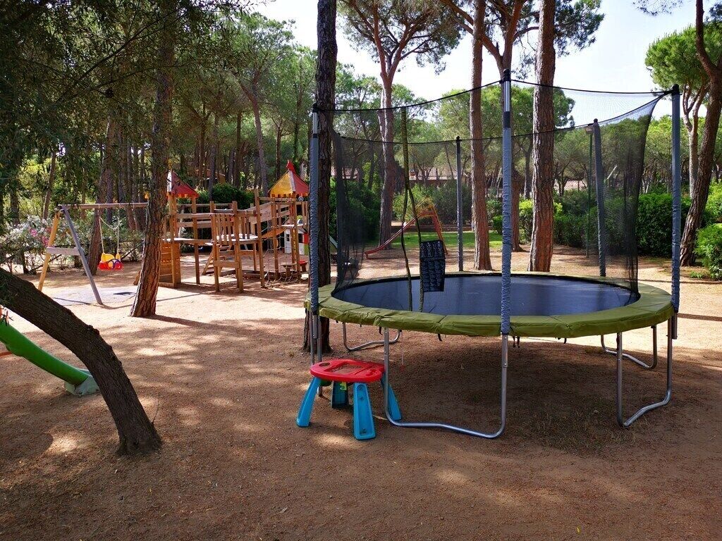 Un'area giochi con un trampolino, altalene e uno scivolo.