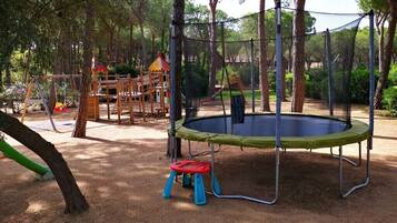 Un'area giochi con un trampolino, altalene e uno scivolo.