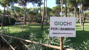 A sign for a children's playground named "GIOCHI PER I BAMBINI" in a park with trees and a swing set. - 100 meters from the sea Villa immersed in the greenery (Santa Margherita di Pula)