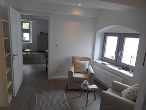 A modern living room with a sofa, armchair, and a small table. There is a window with a view of the outside.