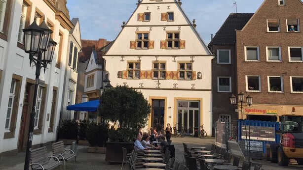 Ein traditionelles europäisches Gebäude mit auffälligem Satteldach, einem zentralen Eingang und einem Innenhof mit Außenbestuhlung.