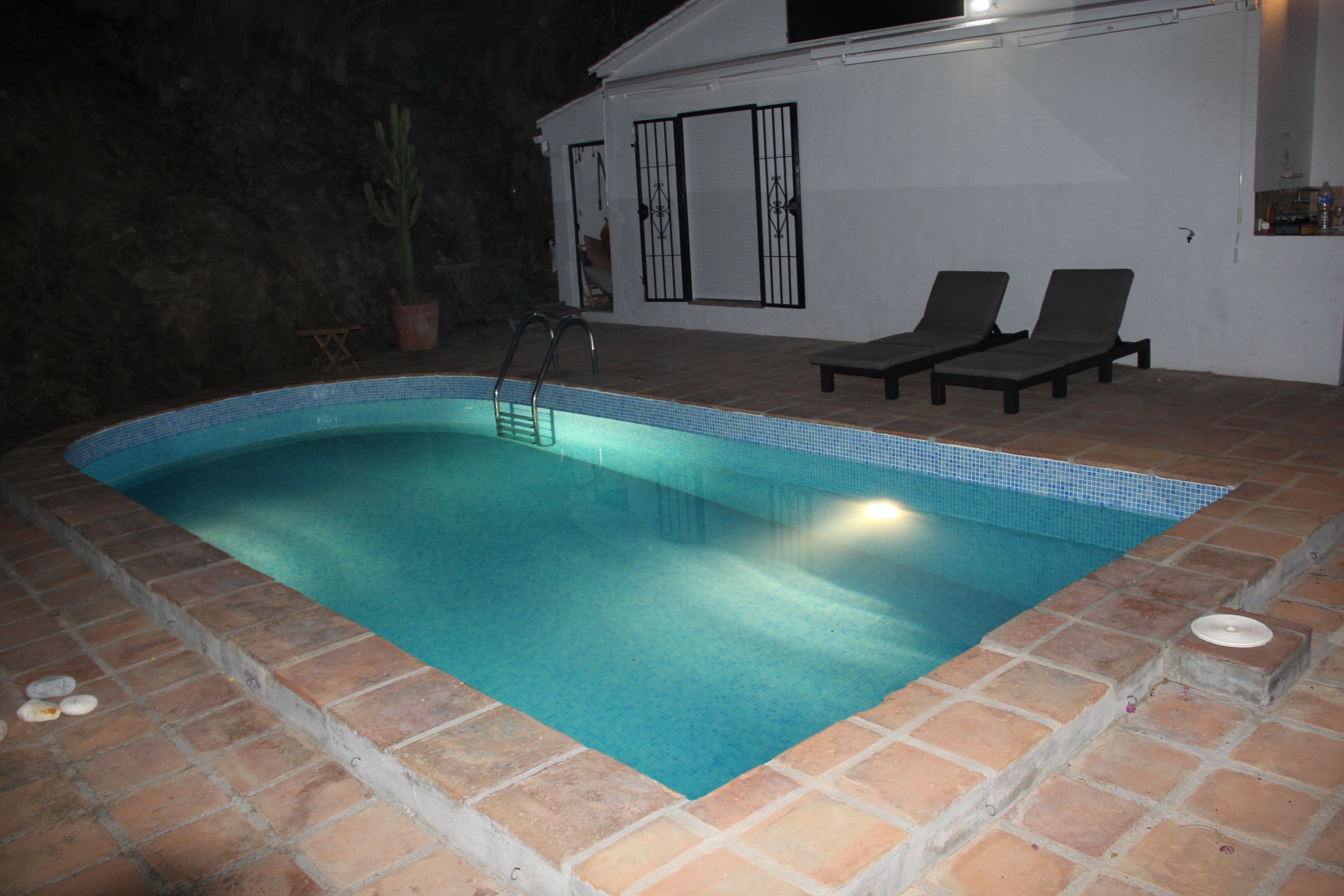 Una piscina interior con borde de azulejos, una escalera y dos sillas de descanso.