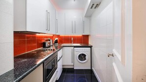 Une cuisine de taille réduite avec des meubles blancs, un lave-linge et un pare-feu rouge en carreaux.