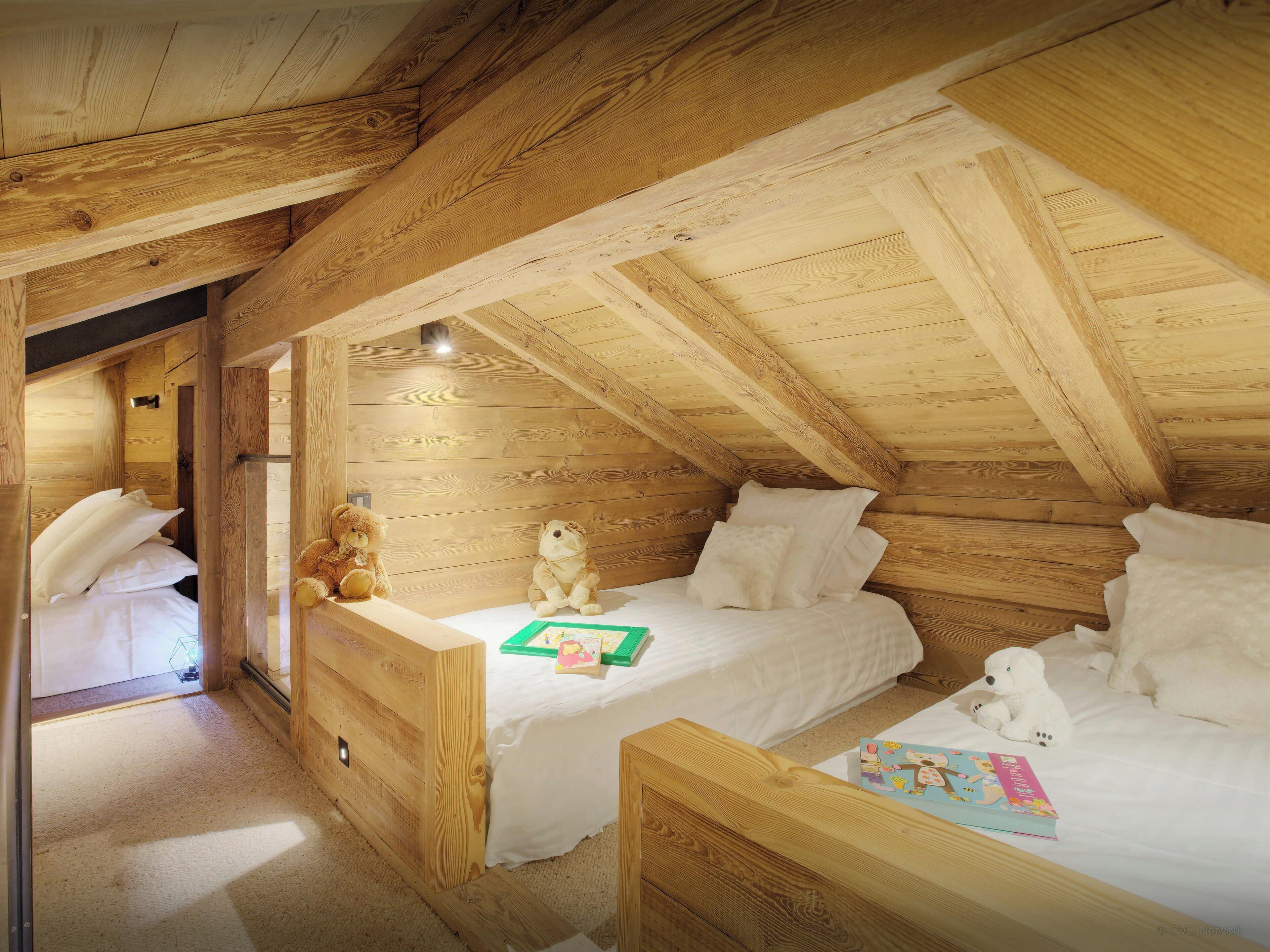 A cozy attic bedroom with wooden beams, two beds, and stuffed toys.