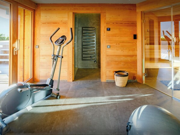 A gym with exercise equipment, a wooden wall, a door, and a glass door leading outside. - Chalet Stellaone - French Alps base for 12, spa & views - OVO Network (La Clusaz)