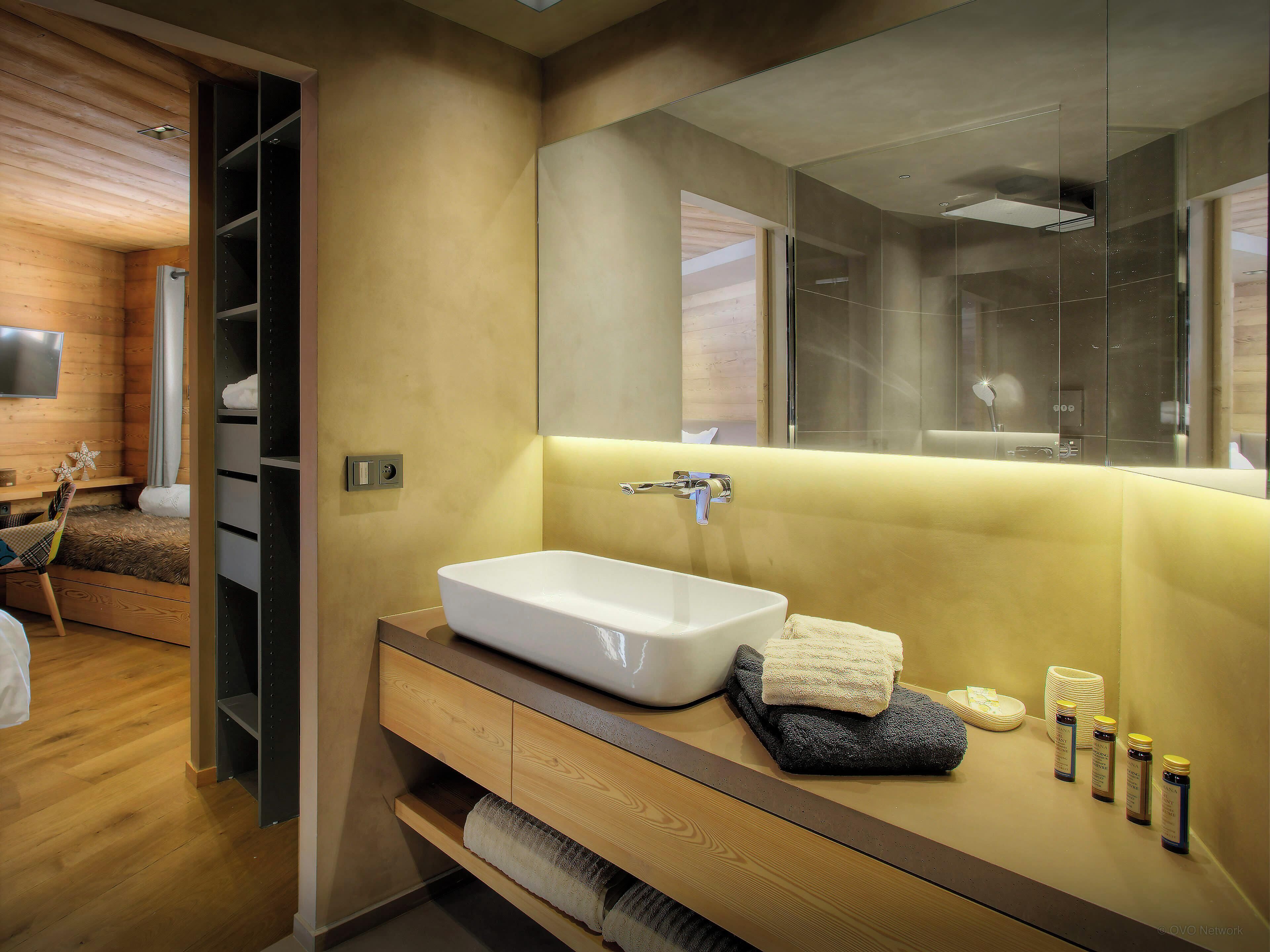 Un baño moderno con un espejo grande, un lavamanos blanco y un mueble de tocador de madera.