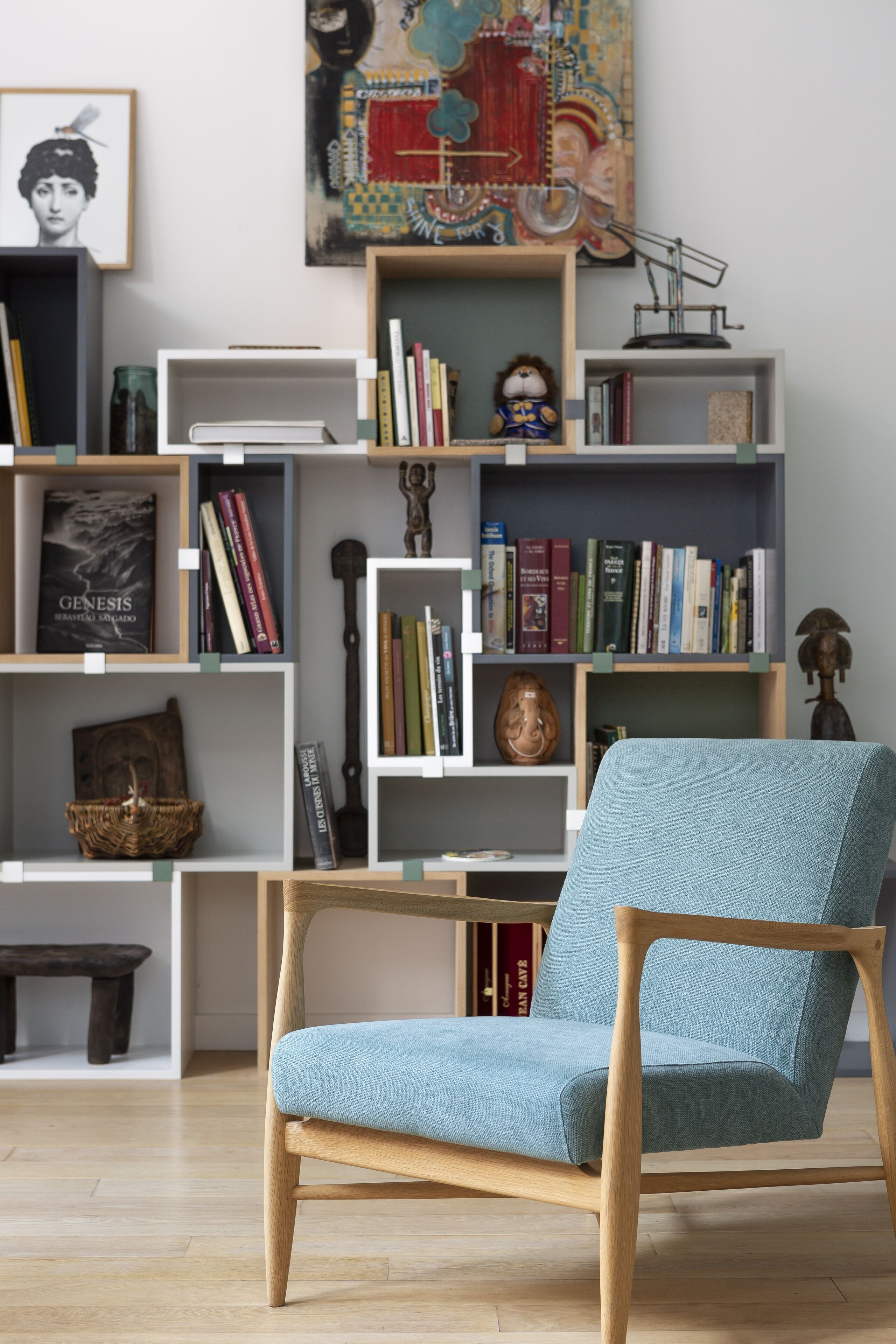 A modern living room with a light blue armchair, wooden bookshelves filled with books and decorative items, and a wooden coffee table.
