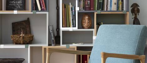 A modern living room with a light blue armchair, wooden bookshelves filled with books and decorative items, and a wooden coffee table.