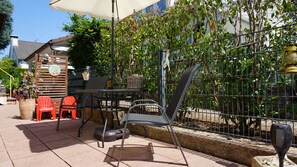 Relax in the serene outdoor patio area, complete with a table, chairs, and a hanging chair, surrounded by lush greenery and a small grill.