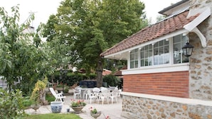 Ein Steinhaus mit Ziegeldach, einer Terrasse mit weißen Stühlen und Tischen sowie Blumentöpfen.